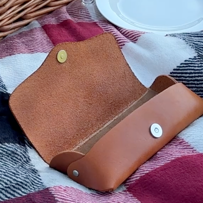 Picnic basket and dishes with an open sunglass case on a blanket.